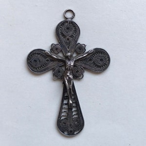Puede incluir: Un colgante de cruz de filigrana de plata con una representación detallada de Jesucristo en la cruz.