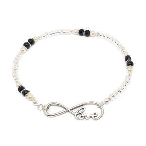 May include: A silver infinity charm bracelet with the word "love" inscribed on it. The bracelet is made with white and black beads.