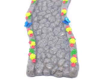 Fairy garden miniature granite path with pink and yellow flowers and blue butterflies.