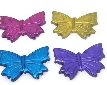 May include: Four butterfly-shaped ornaments in metallic finishes. The top left is magenta, the top right is gold, the bottom left is bright blue, and the bottom right is purple. Each butterfly features embossed wing details and a central body.
