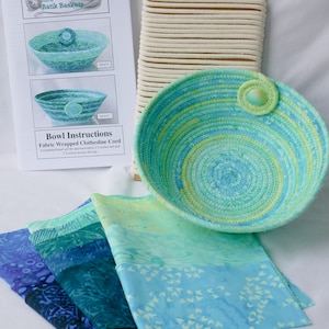 May include: A coiled fabric bowl in shades of blue and green with a matching button accent, a spool of white clothesline cord, and folded batik fabric strips. An instruction sheet titled Bowl Instructions Fabric Wrapped Clothesline Cord is included.