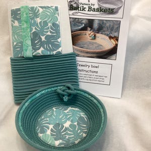 May include: A teal rope bowl with a fabric bottom featuring a tropical leaf pattern. The image includes a bundle of teal rope, fabric with a leaf pattern, and instructions for making a jewelry bowl.