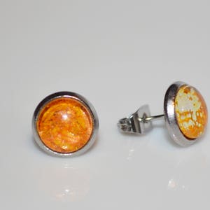 Puede incluir: Un par de pendientes de bot&oacute;n de plata con cabujones de resina naranja y blanca. Los cabujones tienen un aspecto moteado y veteado.