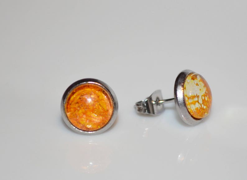 Puede incluir: Un par de pendientes de bot&oacute;n de plata con cabujones de resina naranja y blanca. Los cabujones tienen un aspecto moteado y veteado.
