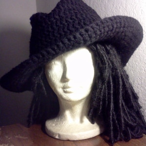 May include: A black crocheted hat with a wide brim, worn on a mannequin with long black dreadlocks.