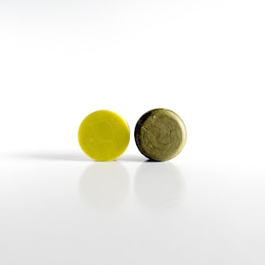 May include: Two round soap bars, one yellow and one green, on a white surface.