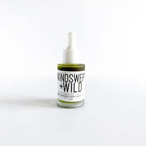 May include: A green glass bottle with a white dropper top. The bottle is labelled "WIND SWEPT + WILD" and contains a hair oil. The label also lists the ingredients: "ORGANIC NETTLE, HORSESAIL, LAVENDER, & MORE".