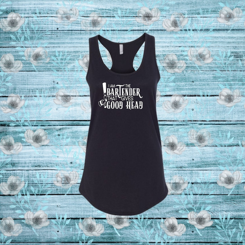 May include: Black racerback tank top with white text that reads "I am the bartender that gives good head." The shirt has a scoop neck and a curved hem. The background is a light blue wood pattern with white floral accents.