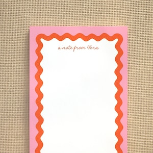 May include: Pink notepad with a scalloped orange border. The notepad has the text "a note from Vera" printed on the top.