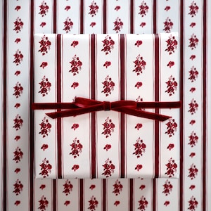 May include: A white gift box with a red and white striped pattern and red floral designs. The box is tied with a red velvet ribbon.