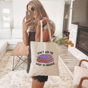 May include: A white tote bag with the text "Don't Ask Me What I'm Reading" and a stack of books with the text "definitely smut", "The Sputtiest Smut", and "Even More Smut Lol" on the front.
