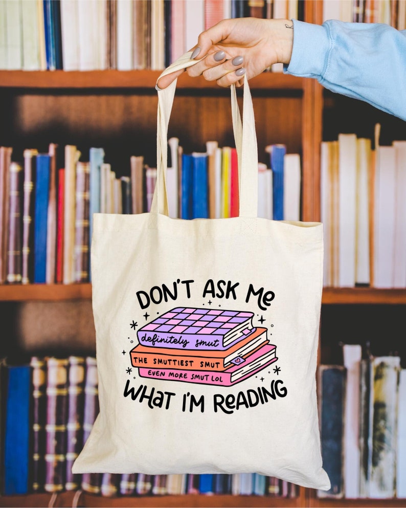 May include: A white canvas tote bag with the text "DON'T ASK ME" and a stack of books with the text "definitely smut", "THE SMUTTIEST SMUT", and "EVEN MORE SMUT LOL" on the front.