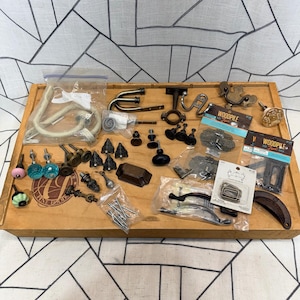 May include: A wooden tray filled with various hardware items, including cabinet knobs, pulls, and hooks. The knobs come in various colors and designs, including glass, ceramic, and metal. The hardware is in various finishes, including bronze, black, and gold.