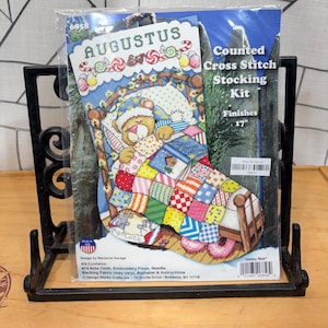 May include: A counted cross stitch stocking kit featuring a sleeping bear design. The kit includes #14 Aida cloth, embroidery floss, and a needle. The finished stocking measures 17 inches.
