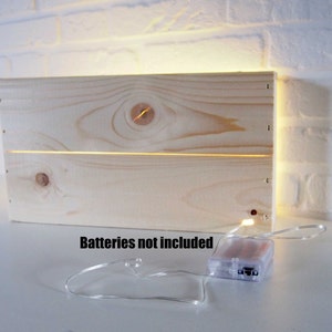 May include: A wooden box with a light string of LED lights inside. The box is made of natural wood and has a rustic look. The lights are battery operated and the text "Batteries not included" is visible below the box.