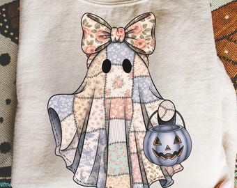 May include: A light beige sweatshirt featuring a whimsical ghost design. The ghost is adorned with a patchwork quilt-like pattern in pastel colors and a floral bow. It holds a gray jack-o'-lantern bucket, perfect for Halloween.