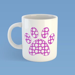 May include: A white ceramic mug featuring a large, magenta-colored paw print graphic on the front. The paw print design is filled with a pattern of small, white circular dots throughout the entire shape of the animal paw print.