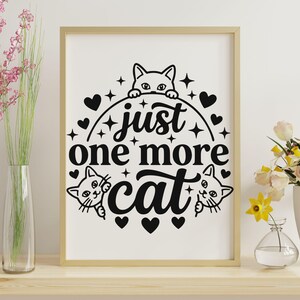 May include: A framed wall art print featuring a black graphic design on a white background. The design includes three cat illustrations and the text "just one more cat" surrounded by small heart and star shapes, all enclosed in a light wood frame.