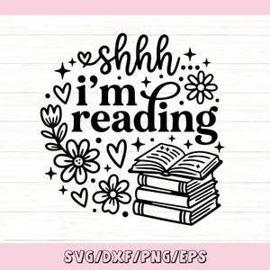 May include: A black and white graphic design featuring the text shhhh i'm reading in a stylized font. The design includes illustrations of a stack of three books, flowers, hearts, and small stars arranged in a circular pattern on a white background.