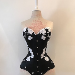 May include: A black corset with white floral embroidery. The corset has a sweetheart neckline and a boned structure.