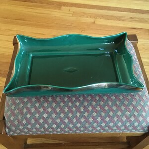 May include: A green ceramic serving tray with a wavy edge. The tray is sitting on a wooden stool with a patterned fabric seat.