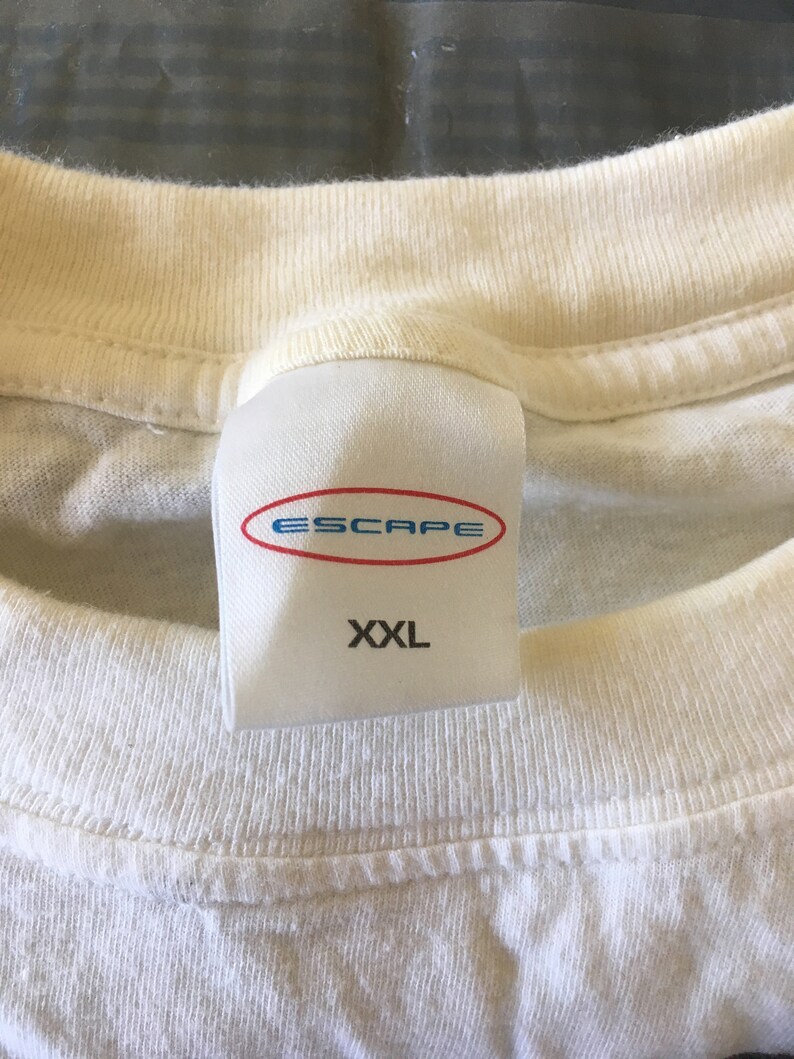 Pode incluir: Camiseta branca com uma etiqueta branca que diz "Escape" em letras azuis e "XXL" em letras pretas.