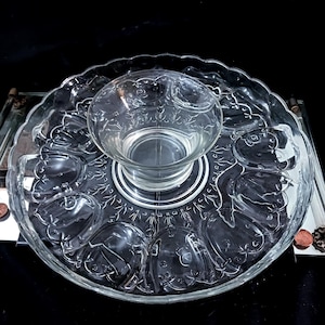 May include: A clear glass serving platter with a central bowl and multiple compartments. The platter has a scalloped edge and is decorated with floral patterns. The bowl is elevated and has a similar floral design. Ideal for serving snacks or appetizers.