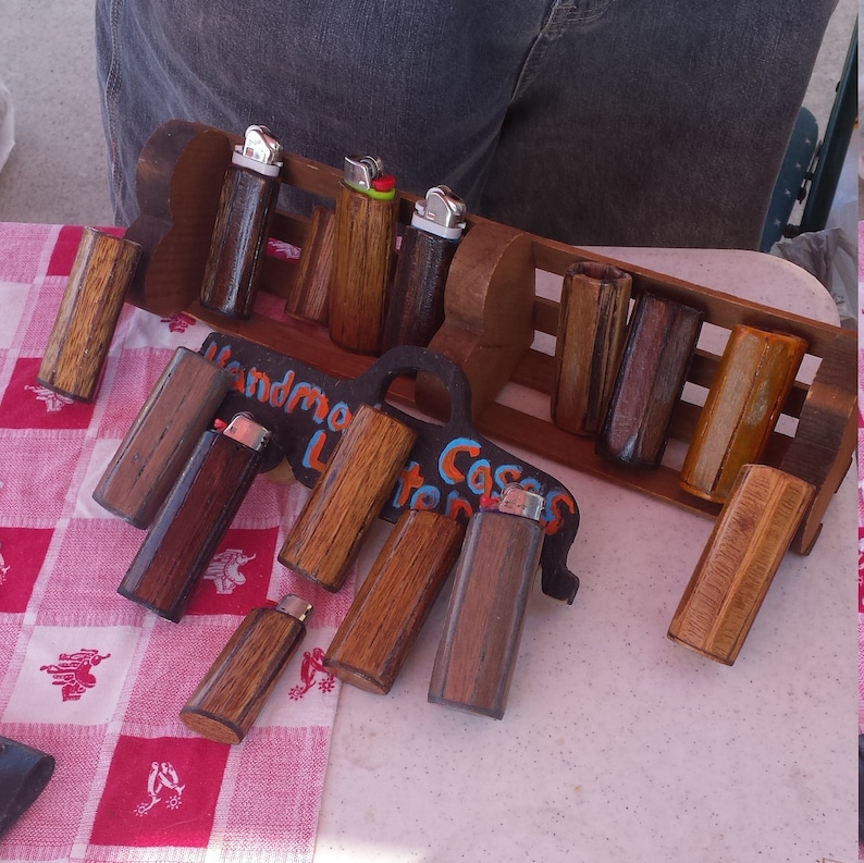 Puede incluir: Una colecci&oacute;n de encendedores de madera con mecanismos met&aacute;licos. Los encendedores se muestran en un estante de madera con el texto "Handmade Lighters" y "Casa Lighters".
