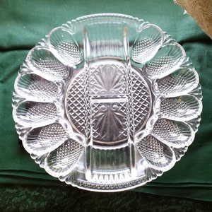 May include: A clear glass egg plate with eight individual compartments and three divided sections. The plate has a decorative, raised, diamond pattern.