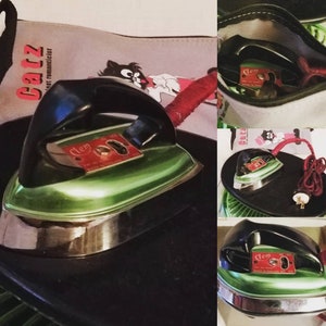May include: A vintage green and black electric iron with a red "Clem" logo. The iron is sitting on a black surface and has a cord.