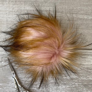 May include: A fluffy pom pom with black, brown, and pink fur. A pair of silver decorative scissors are also in the image.