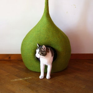 May include: A green felt cat bed shaped like a teardrop with a long, curved stem. A cat is peeking out of the opening of the bed.
