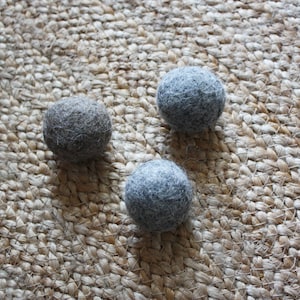 May include: Three grey felt balls on a woven jute rug. The balls are different shades of grey.