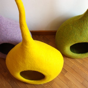 May include: Three felt cat beds in different colors: purple, yellow, and green. The beds are shaped like a teardrop with a large opening at the bottom.