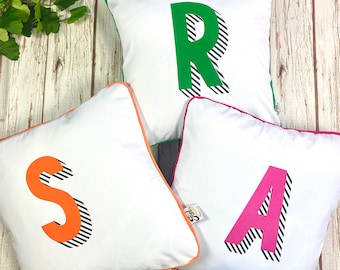 Leuchtendes Buchstabenkissen. Personalisiertes Regenbogen Alphabet Liebhaber Kissen. Monogramm auf weißer Baumwolle. 'Bradford Buzz' Schriftart. Neues Zuhause Geschenk.
