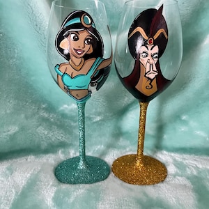 May include: Two hand-painted wine glasses featuring characters from a popular animated film. One glass depicts a princess in teal and black, the other a villain in red and black. The stems and bases are glittered in teal and gold.