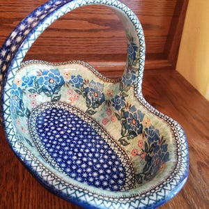 May include: A blue and white ceramic basket with a floral design and a handle. The basket is oval shaped and has a white background with blue and green flowers.