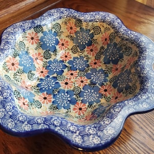 May include: A large, scalloped ceramic bowl with a blue and white floral pattern. The bowl is decorated with pink and blue flowers and swirls.