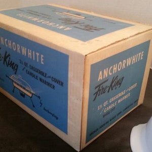 K&ouml;nnte beinhalten: Eine antike Anchorwhite Fire-King 1,5 Liter Auflaufform mit Deckel und einer blauen und wei&szlig;en Schachtel. Die Schachtel tr&auml;gt den Text "Anchorwhite Fire-King 1 1/2 qt. Casserole and Cover Candle Warmer".