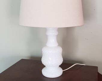 May include: A white milk glass table lamp with a textured base and a white fabric lampshade.