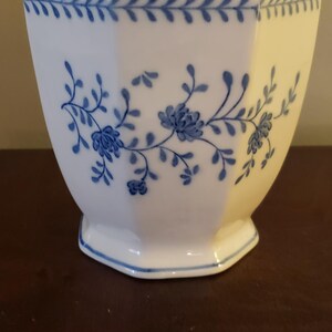 May include: White ceramic bowl with a hexagonal shape and a blue floral design. The bowl has a blue leaf pattern around the rim and floral sprigs on the sides. The base is also outlined in blue.
