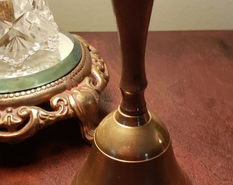 May include: A brass bell with a rounded, flared base and a tall, slender handle. The bell has a polished, golden finish.