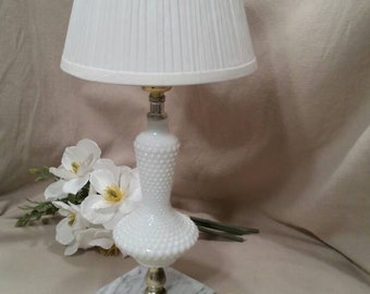 May include: A white milk glass lamp with a white pleated lampshade. The lamp has a marble base and a gold-colored cord.