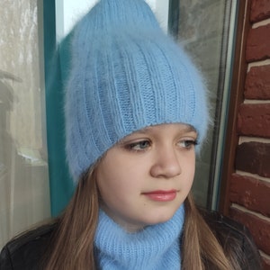 Può includere: Un cappello di lana blu chiaro e soffice abbinato a un maglione a collo alto. Il cappello ha una trama a coste e il maglione ha una vestibilità ampia.