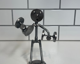 May include: A metal sculpture of a person lifting weights. The sculpture is made of nuts, bolts, and washers. The person has a round head with a face and is holding two dumbbells.