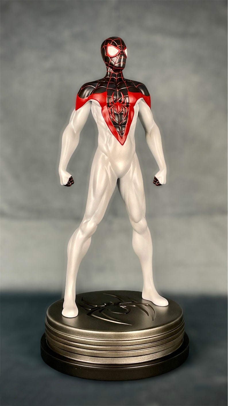 May include: A white and black action figure of Spider-Man with red accents. The figure is standing on a circular base with a spider web design.