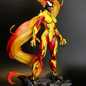 May include: A detailed figurine of a female character with a yellow and red bodysuit. The figure has long, flowing hair in shades of red and yellow. The character is posed on a rocky base with a black background.