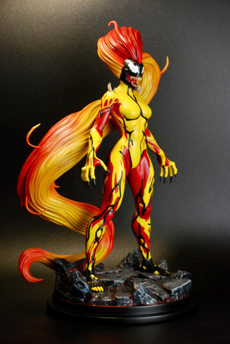 May include: A detailed figurine of a female character with a yellow and red bodysuit. The figure has long, flowing hair in shades of red and yellow. The character is posed on a rocky base with a black background.