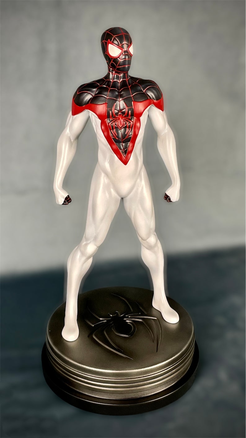 May include: A white and black Spider-Man action figure with red accents. The figure is standing on a black and silver base with a spider logo.