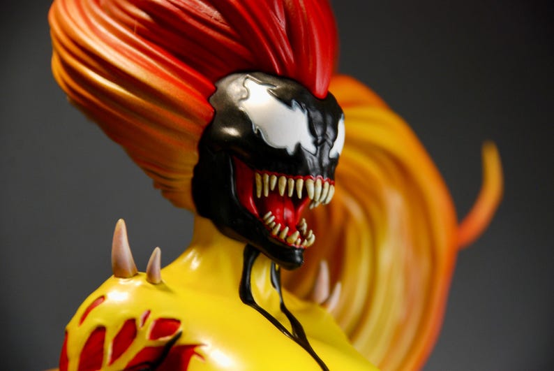 May include: A detailed figurine of a character with a black and white mask, sharp teeth, and fiery red and yellow hair. The figure has a yellow torso with red accents and white spikes.